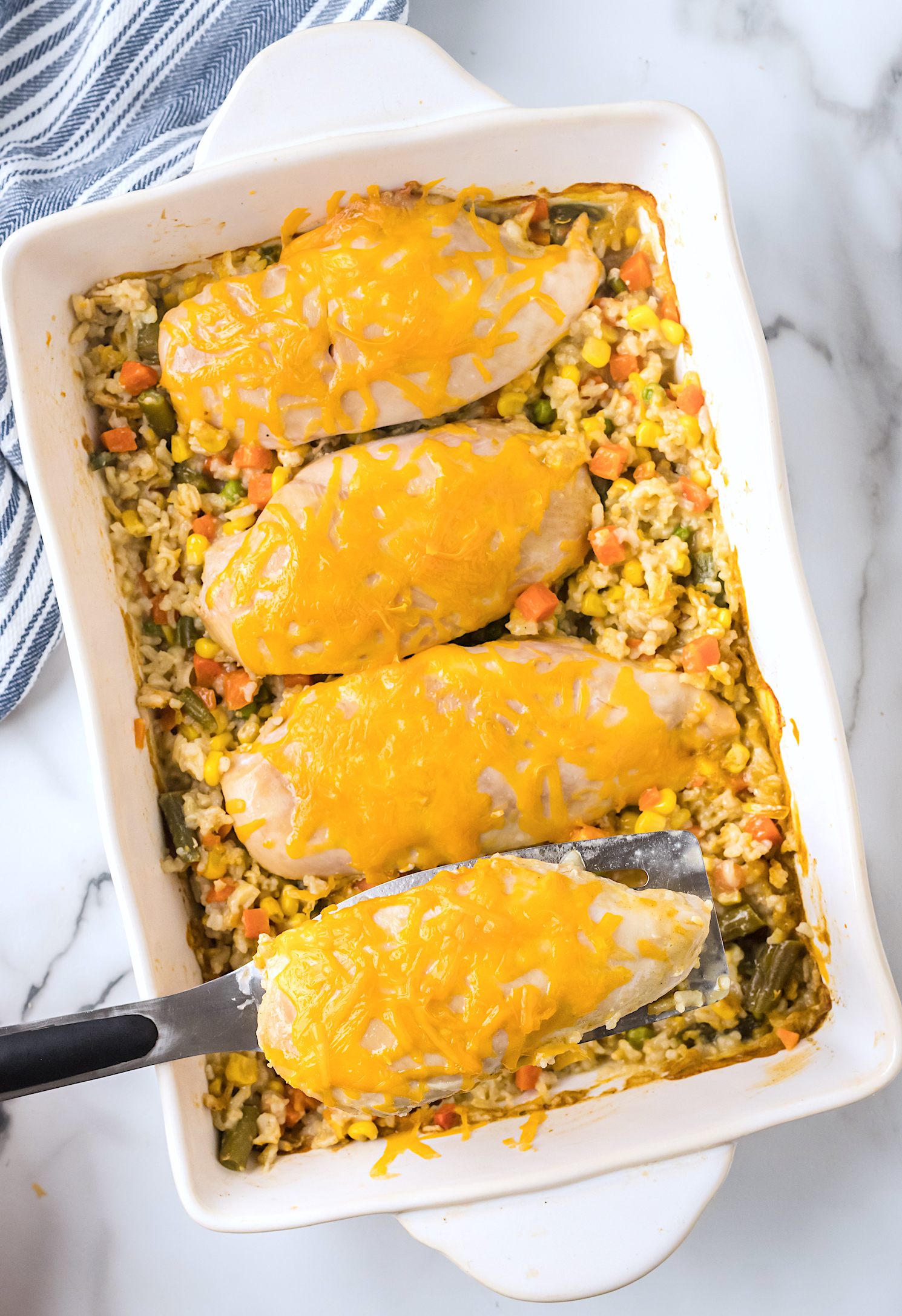 Cheesy Chicken and Rice Bake in white baking dish with blue dish towel