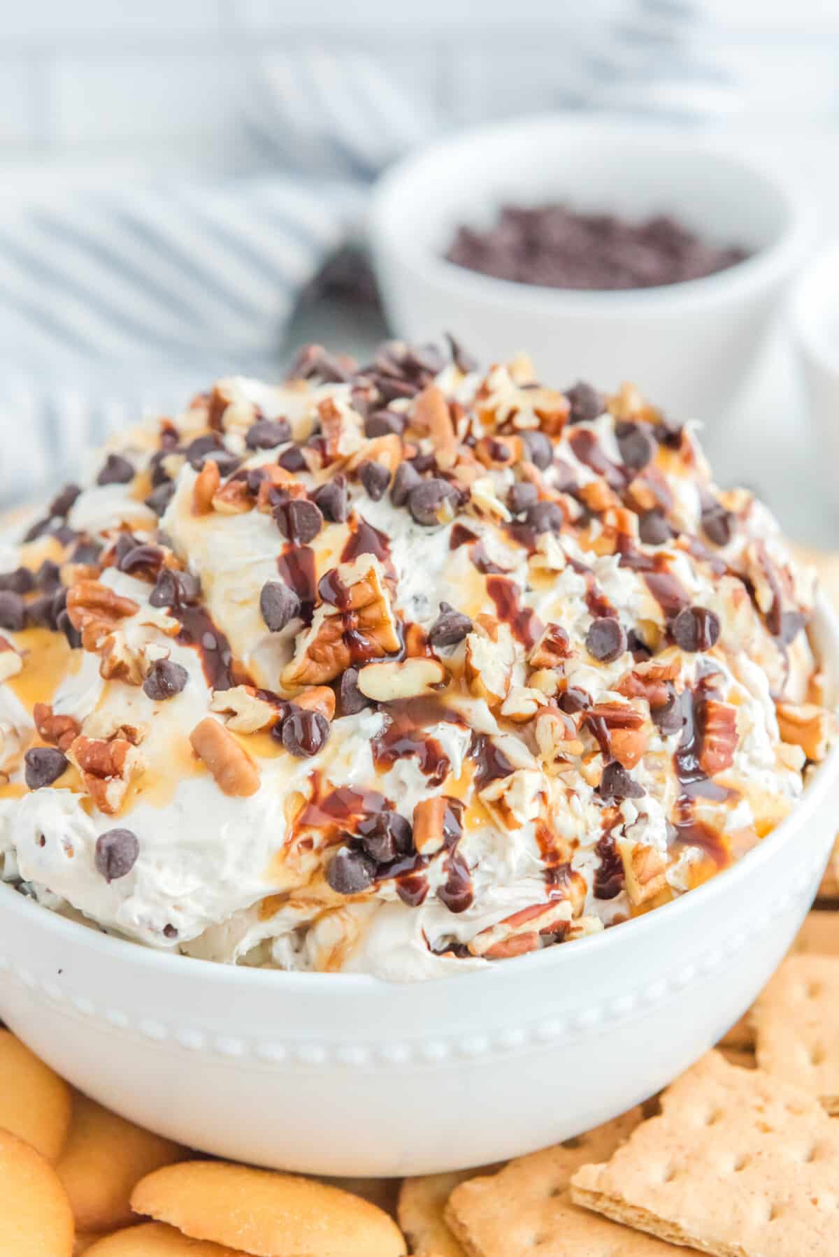 Turtle cheesecake dip with swirls of caramel, chocolate, and pecans, served in a white bowl.