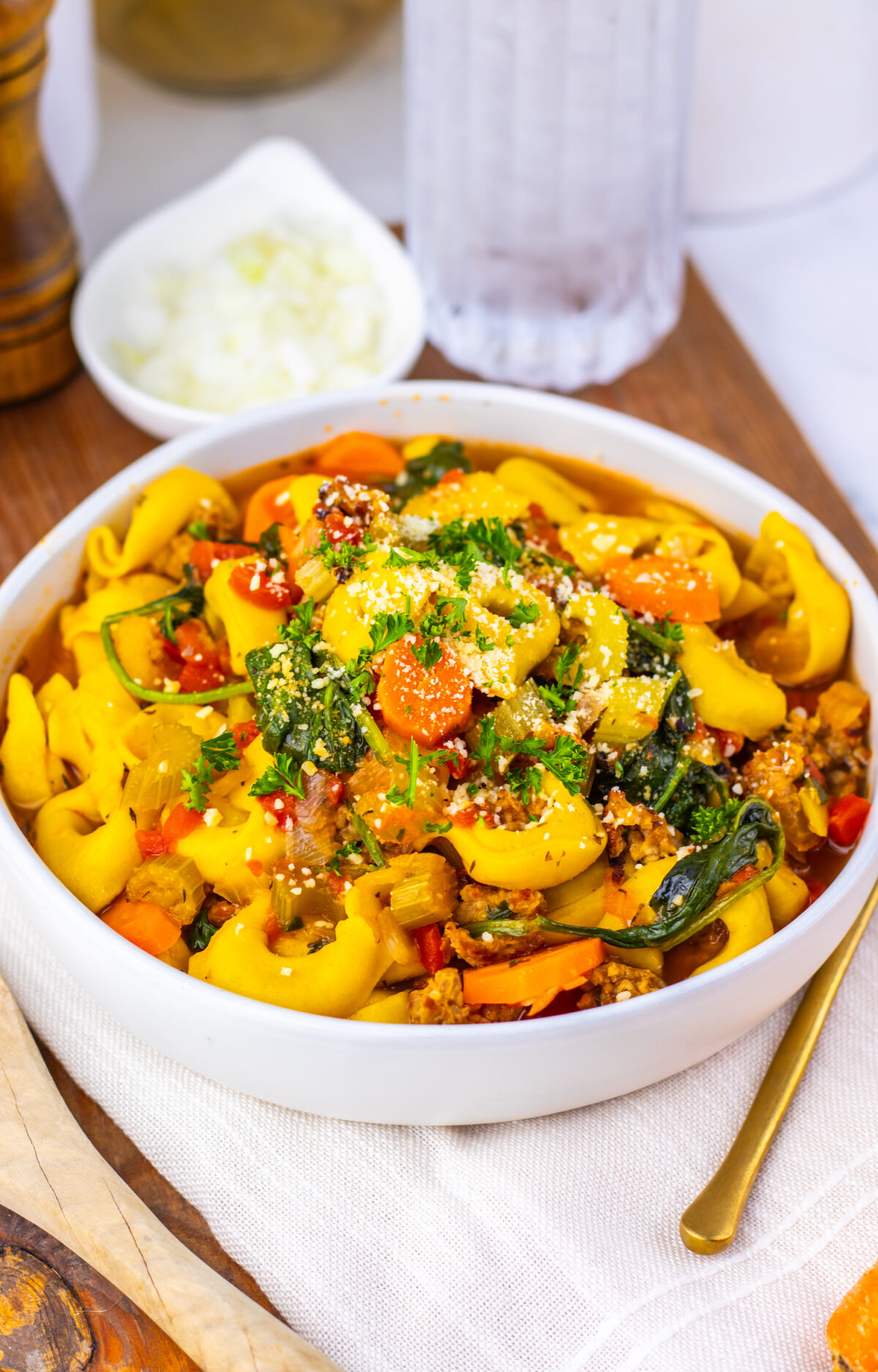 Hearty sausage tortellini soup served in a white bowl with butternut squash and vegetables.