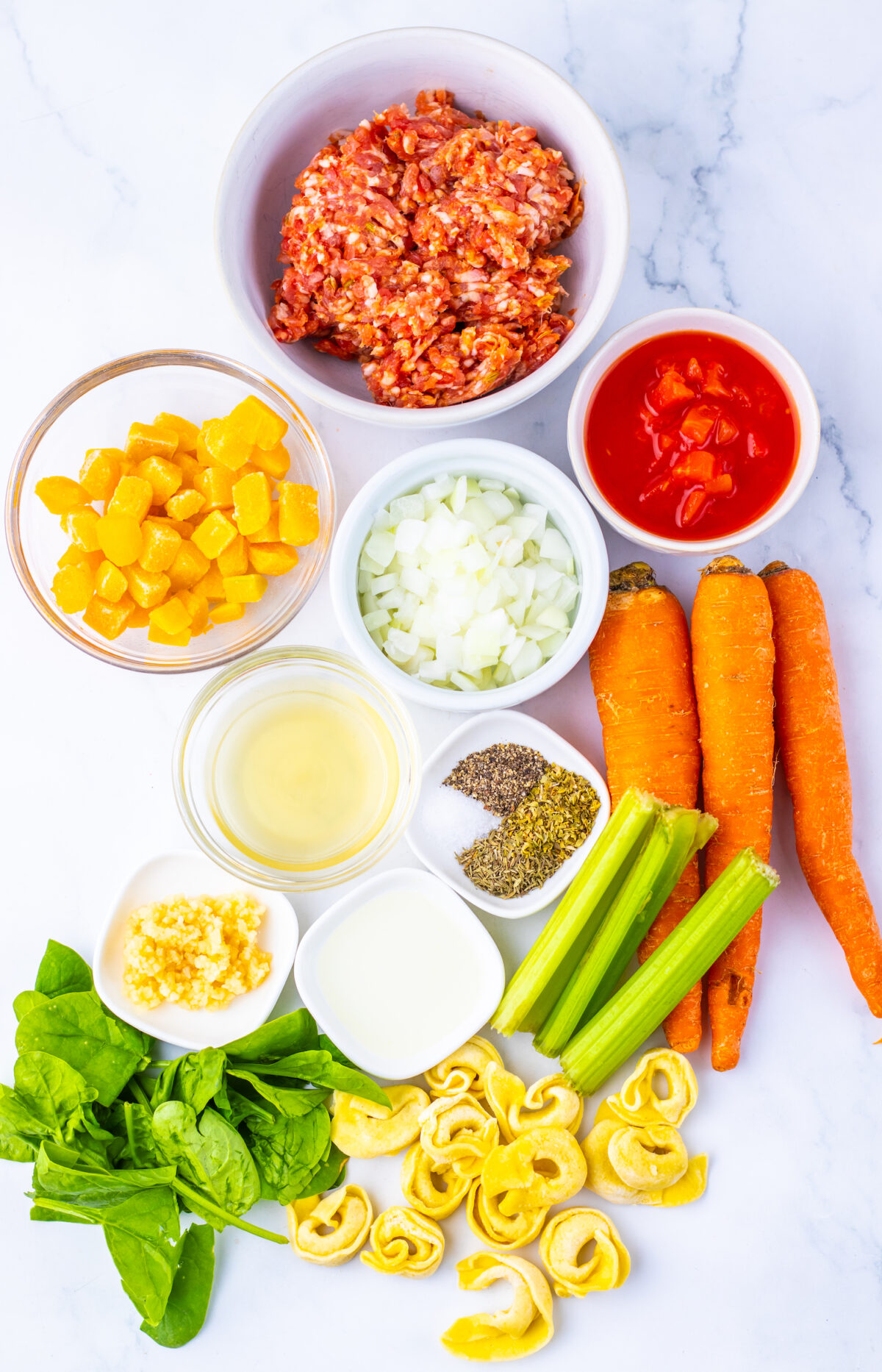 Fresh ingredients for sausage and butternut squash tortellini soup arranged on a counter.